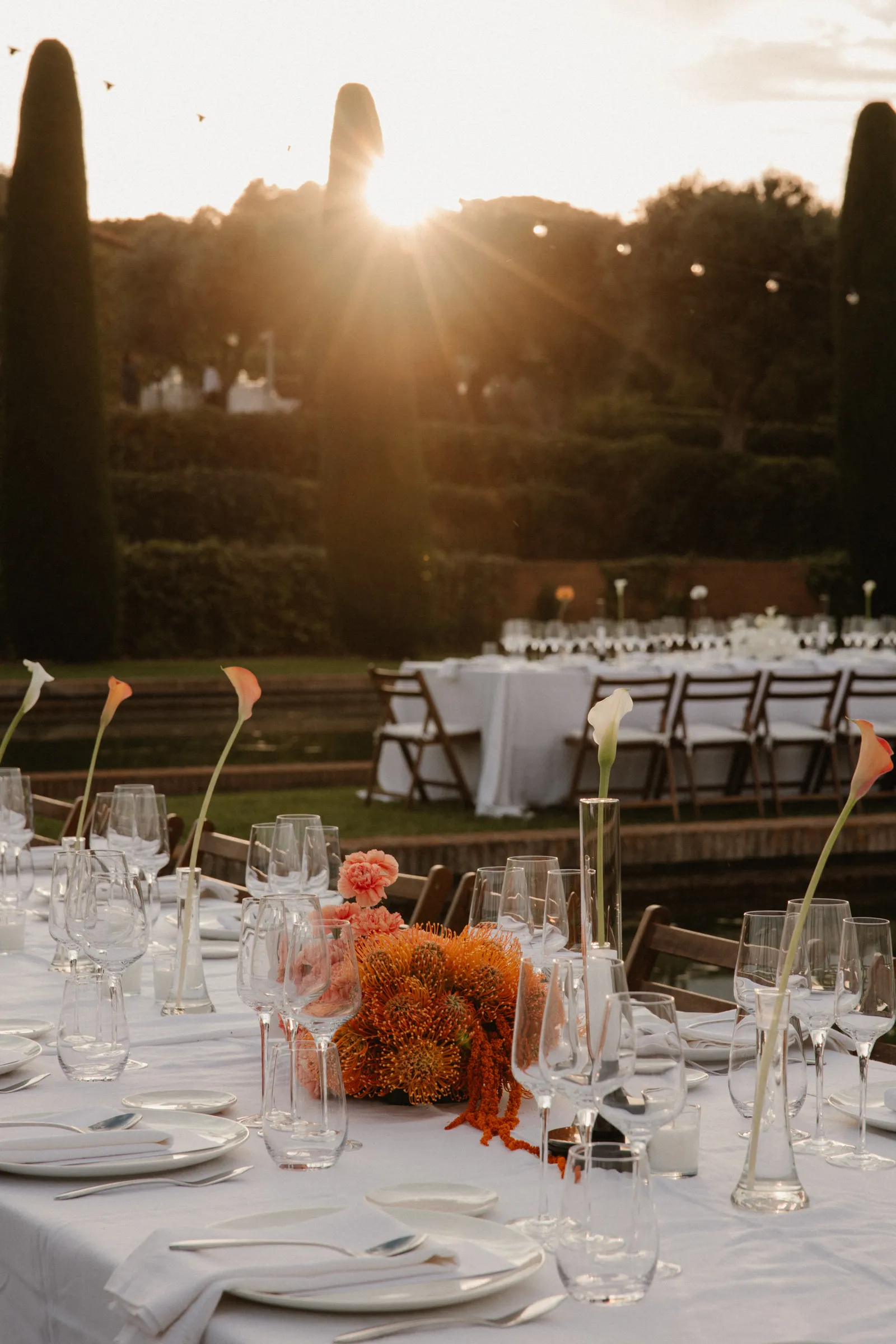 Mesa de boda vestida al atardecer con flores naranjas y copas de cristal